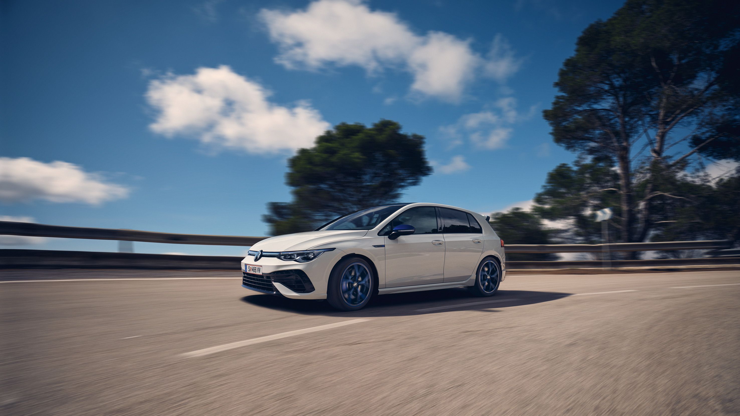 Der aDer weiße VWR Golf R „20 Years“ fährt bei sonnigem Wetter eine Straße entlangneue Golf R von VW dynamisch auf der Straße