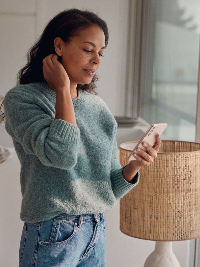 Eine Frau steht am Fenster und blickt auf ihr Smartphone