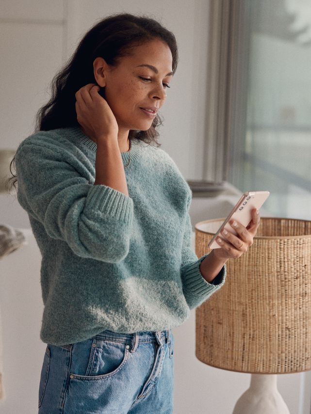 Eine Frau steht am Fenster und blickt auf ihr Smartphone