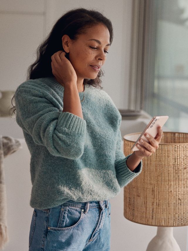 Eine Frau steht am Fenster und blickt auf ihr Smartphone