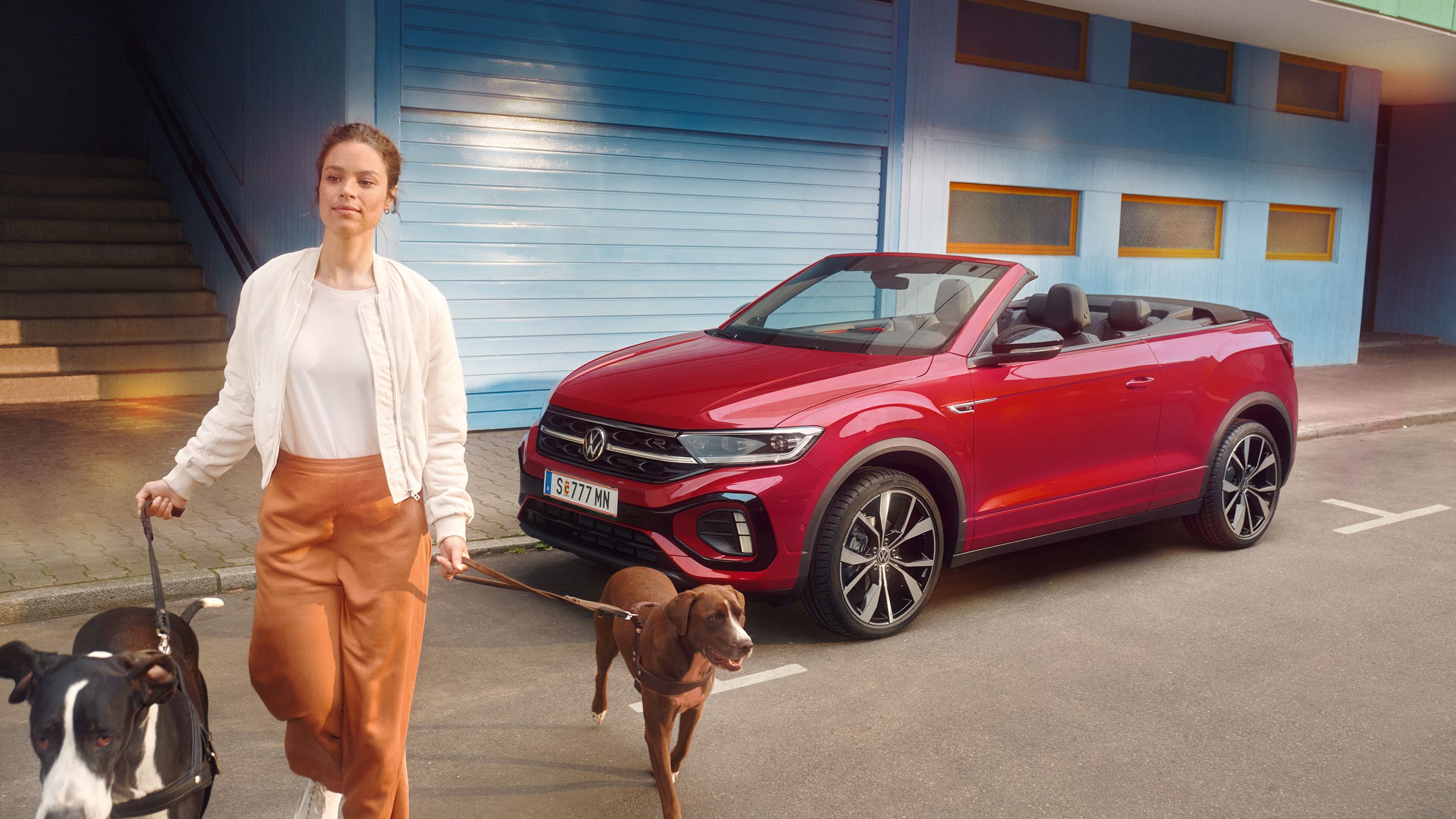 Frau geht mit zwei Hunden and der Leinen von einem roten VW T-Roc Cabrio weg