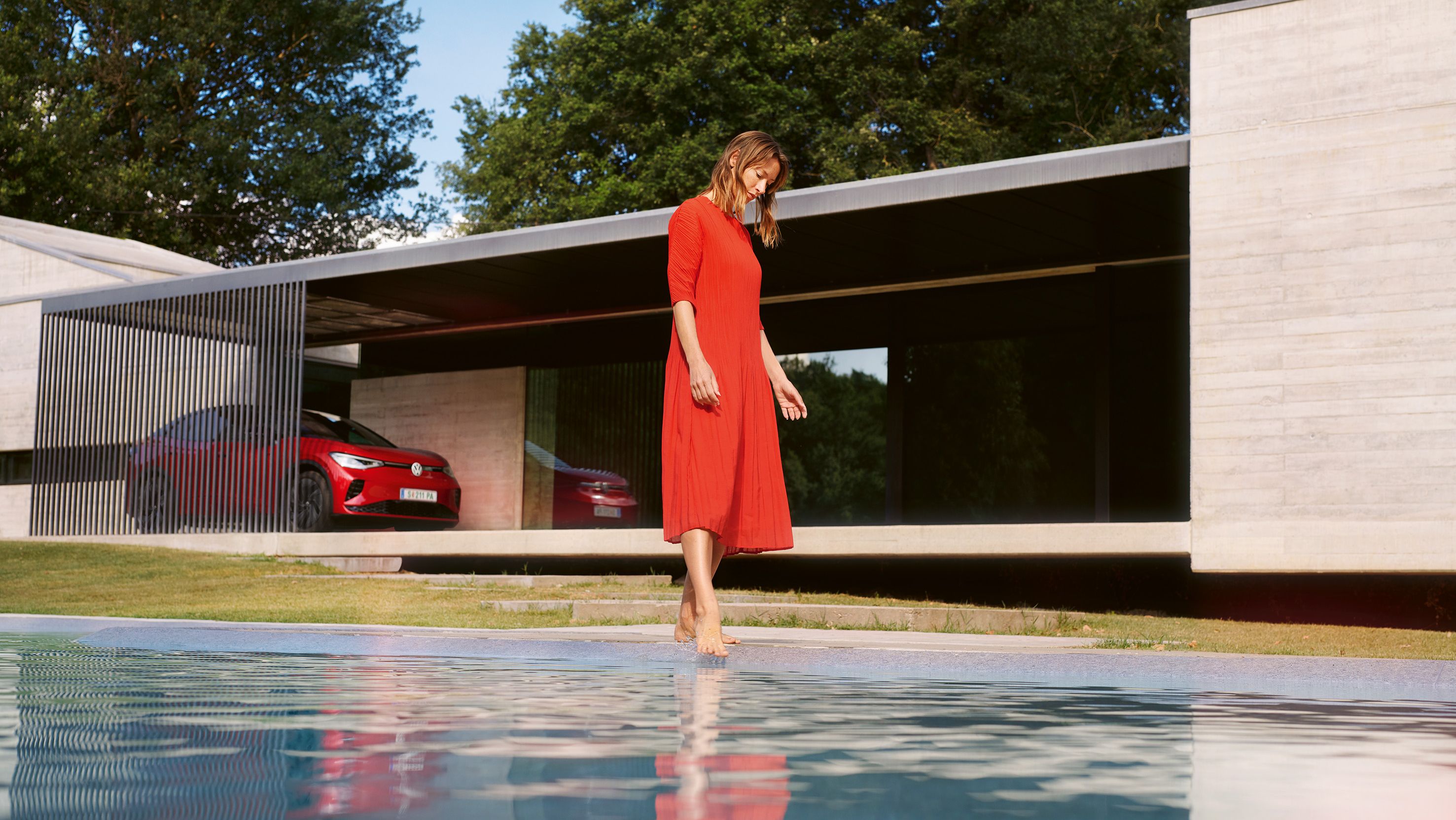 Roter VW ID.5 GTX parkend vor einem Haus. Eine Frau im roten Kleid am Pool.