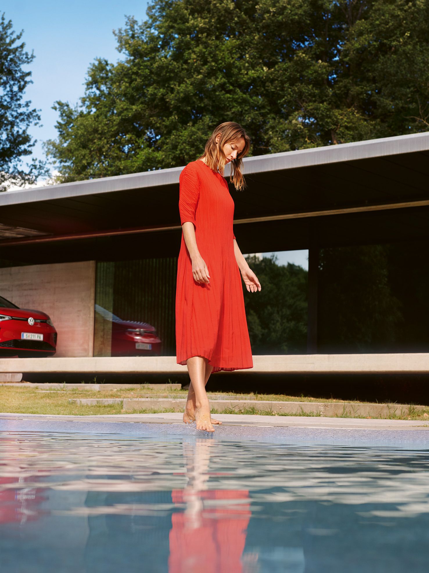 Roter VW ID.5 GTX parkend vor einem Haus. Eine Frau im roten Kleid am Pool.