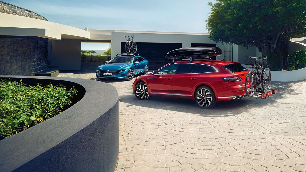 Ein blauer und ein roter VW Arteon mit Fahrradträger parken vor einer Garageneinfahrt