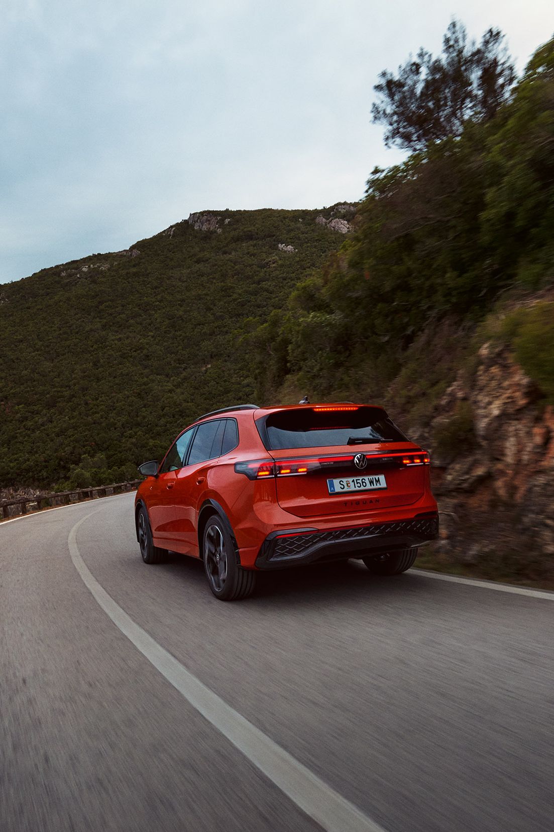 Roter VW Tiguan in Heckansicht fährt durch eine bergige Landschaft.