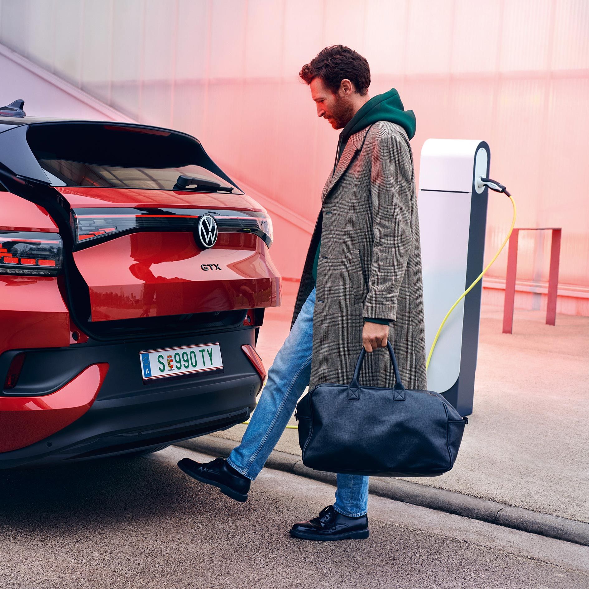 VW ID.4 GTX in Rot von hinten zu sehen, Mann mit Tasche öffnet Heckklappe