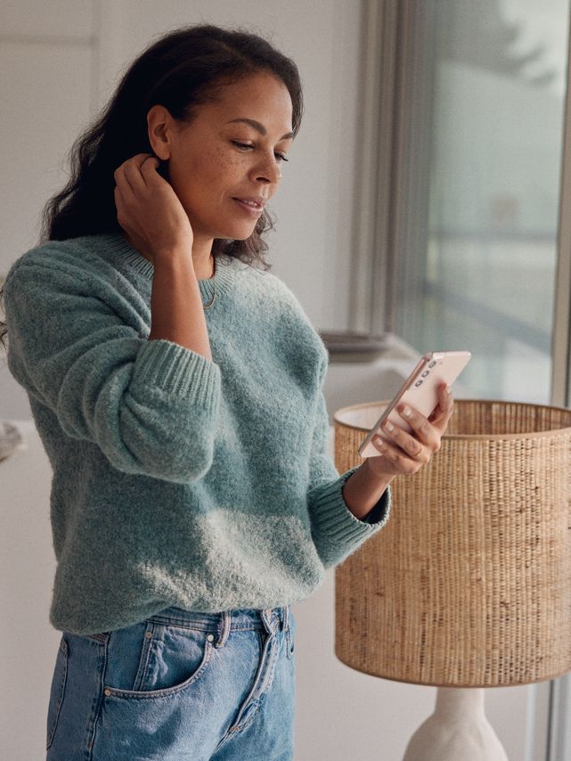 Eine Frau steht am Fenster und blickt auf ihr Smartphone