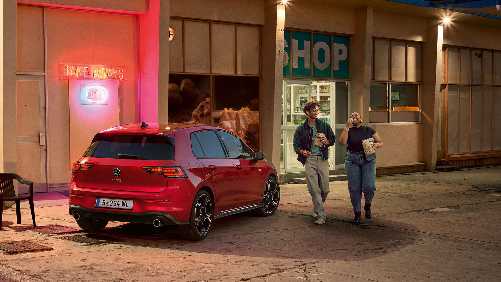 Heckansicht eines roten VW Golf GTI in abendlicher Stimmung, zwei Personen gehen neben ihm her