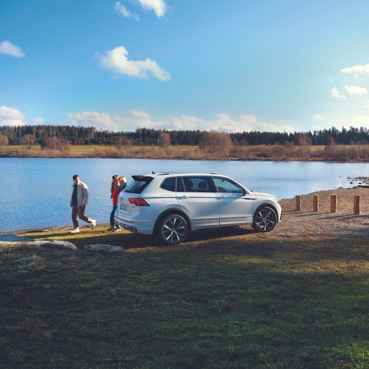 VW Tiguan Allspace steht an einem See, dahinter gehen drei Personen vorbei