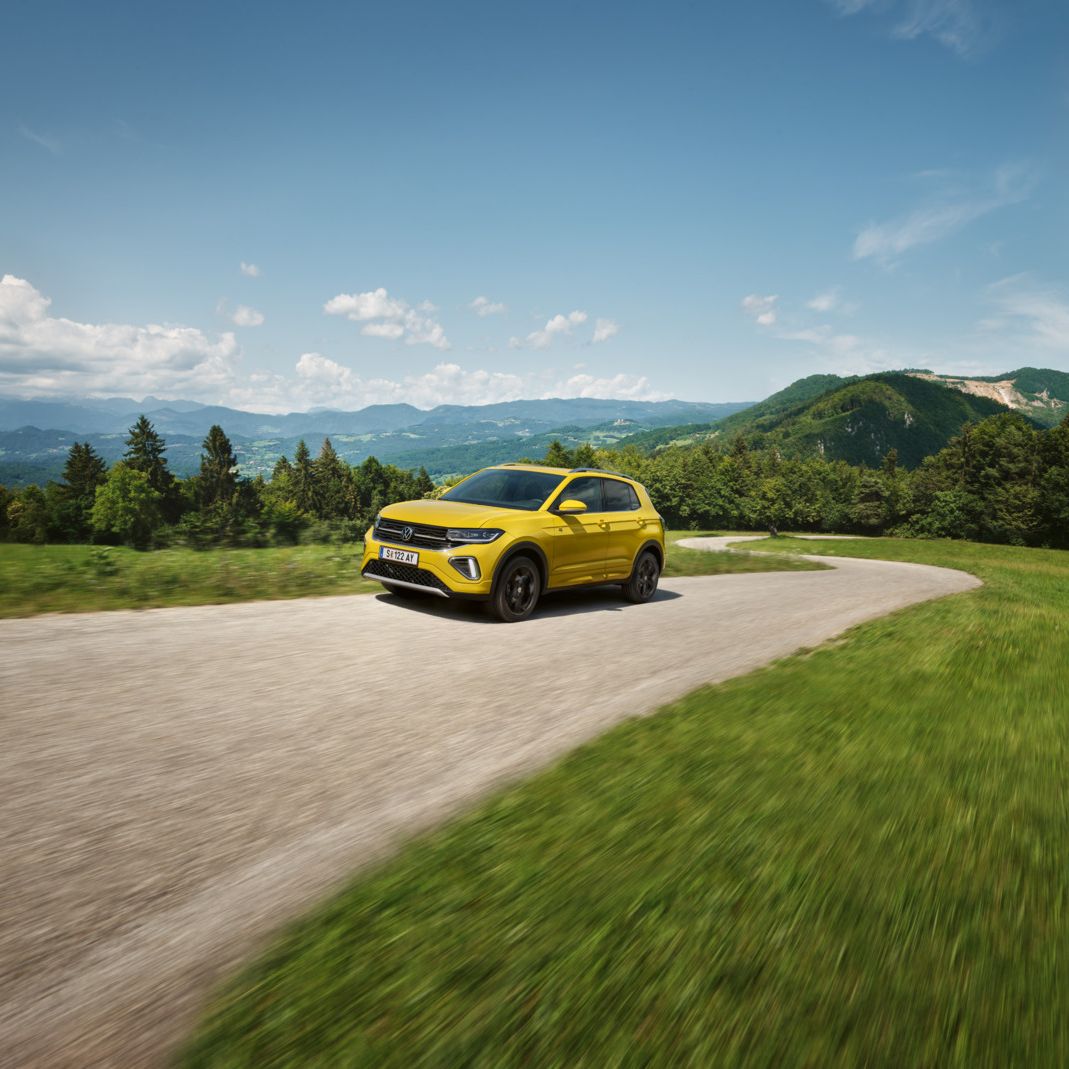 Ein gelber VW T-Cross auf einer Straße in hügeliger Landschaft.