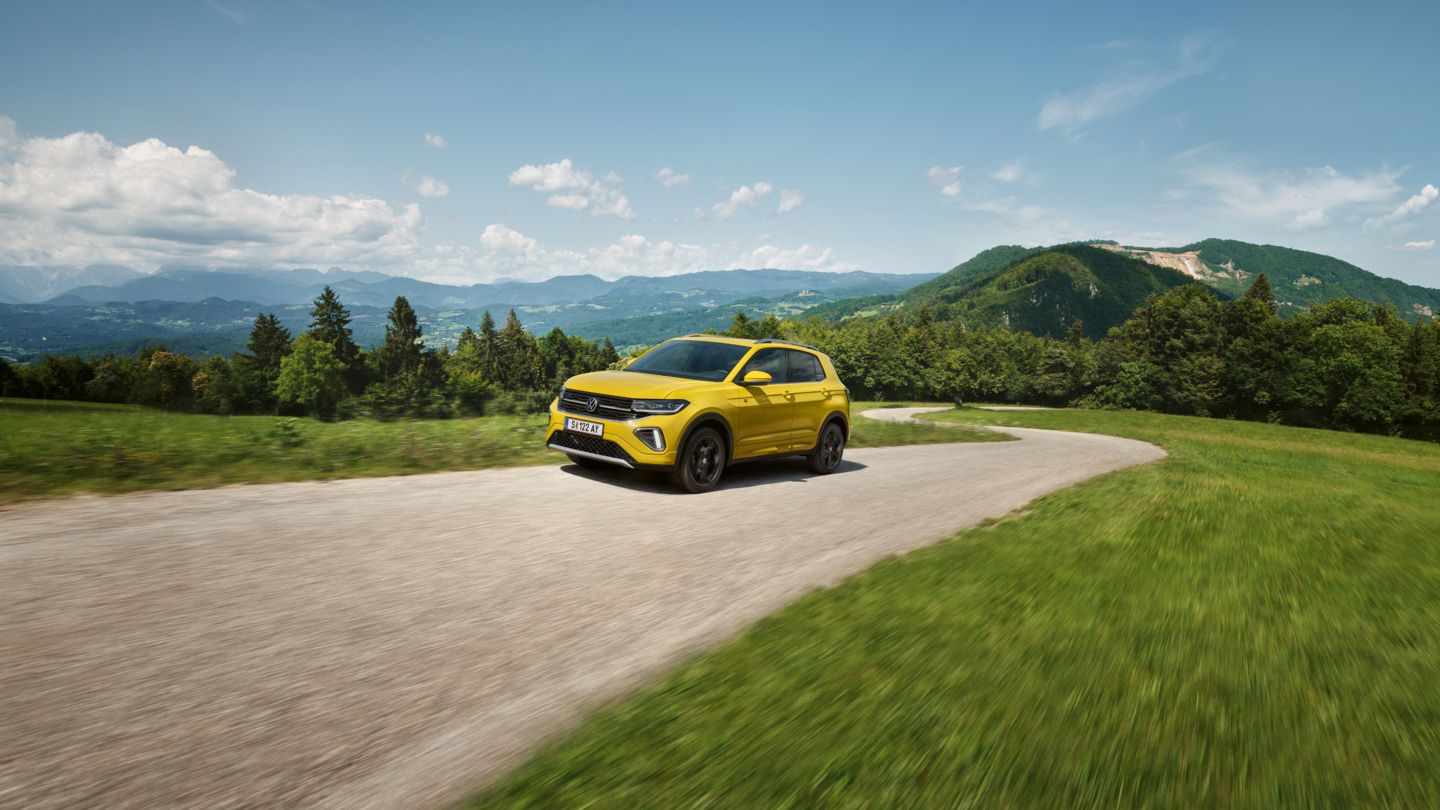 Ein gelber VW T-Cross auf einer Straße in hügeliger Landschaft.