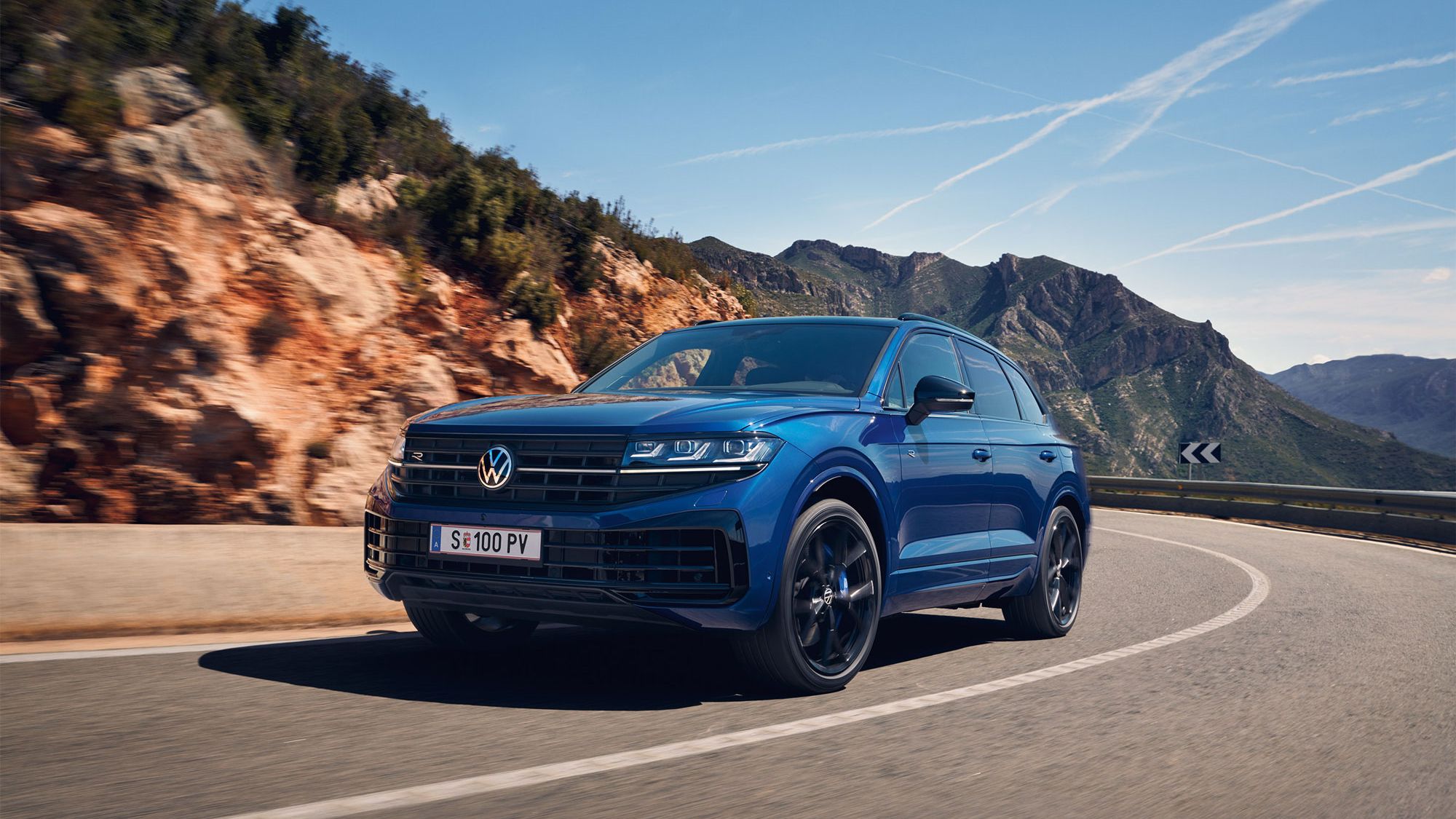 Blauer Touareg eHybrid fährt auf einer Straße durch die Berge