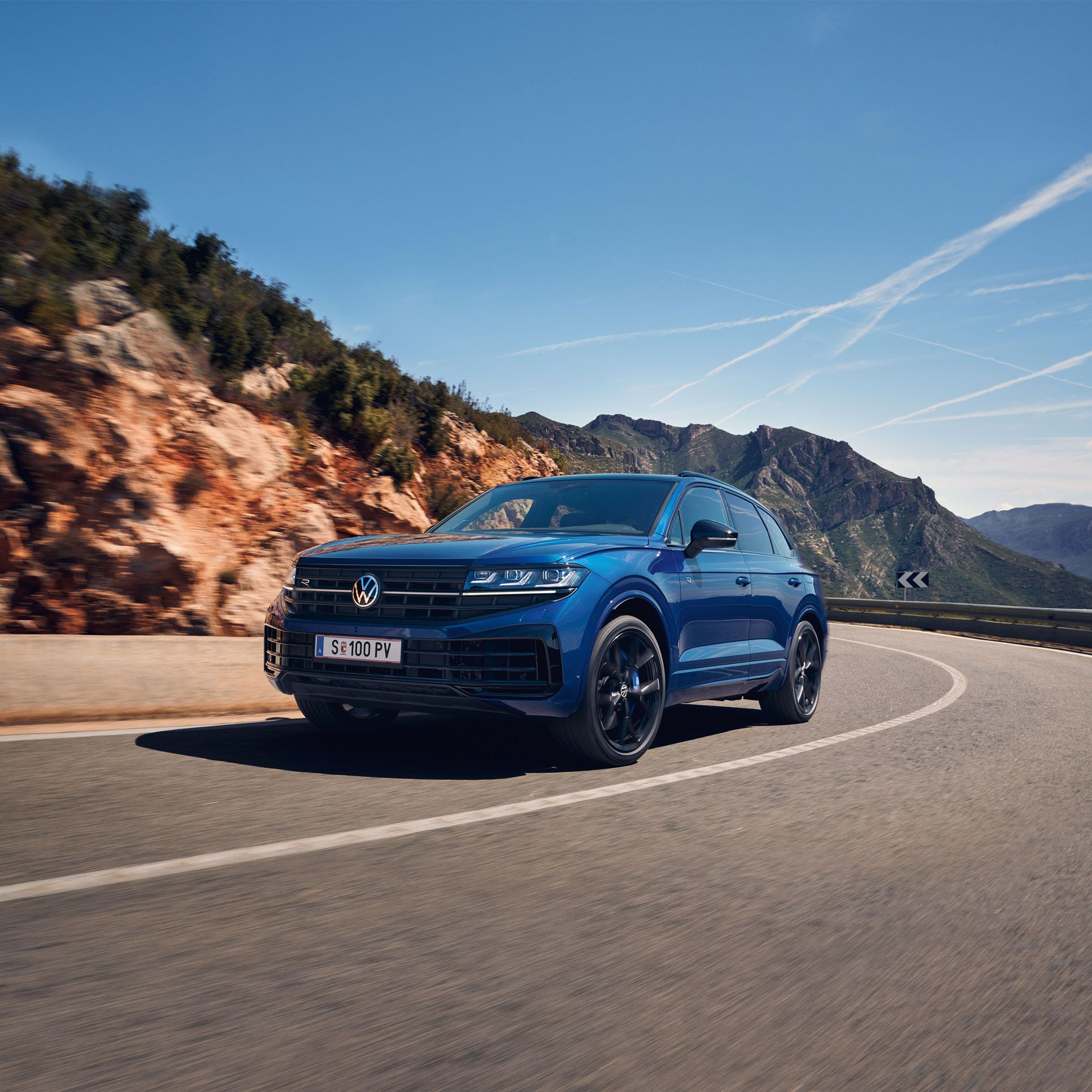 Blauer Touareg eHybrid fährt auf einer Straße durch die Berge