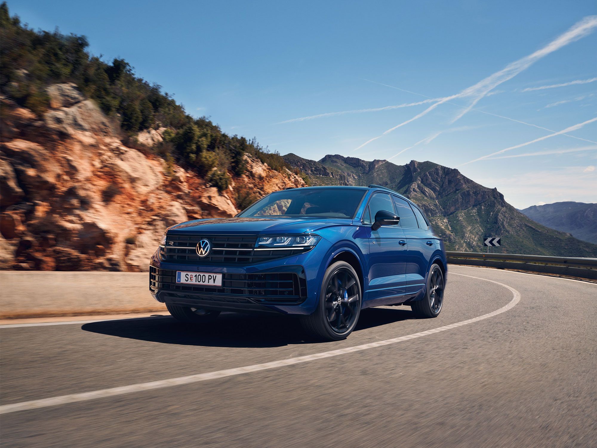 Blauer Touareg eHybrid fährt auf einer Straße durch die Berge