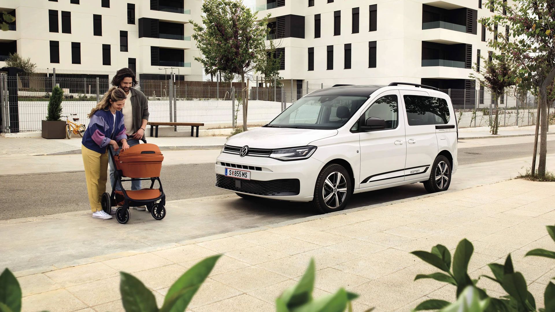 Eine Familie mit Kinderwagen steht vor einem weißen Caddy Edition