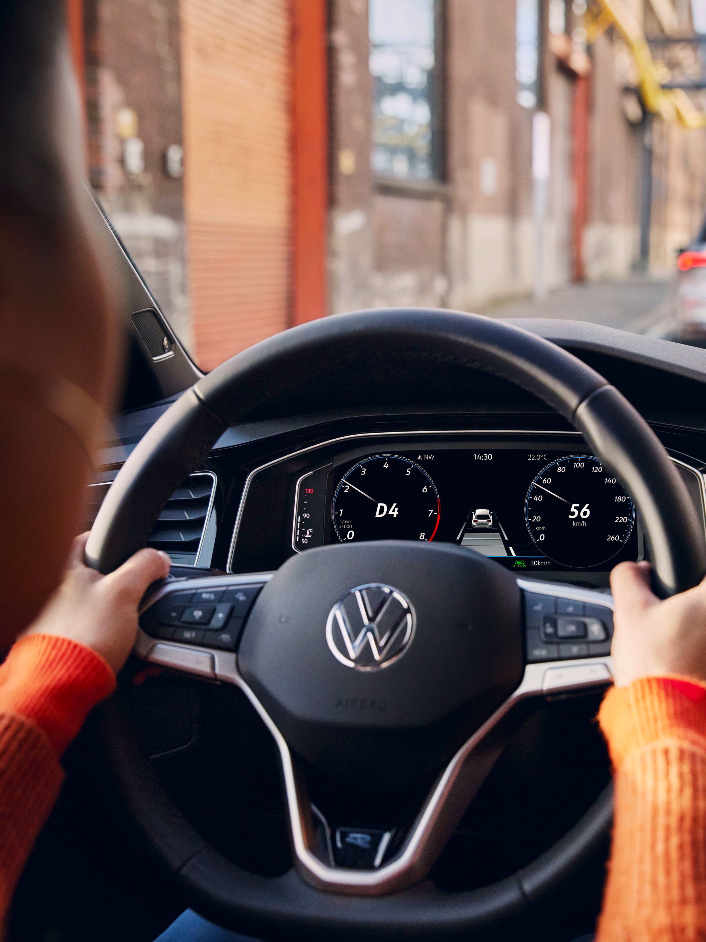 Aktives Navigationssystem auf dem Display eines VW. Frau hat ihre Hände am Lenkrad.