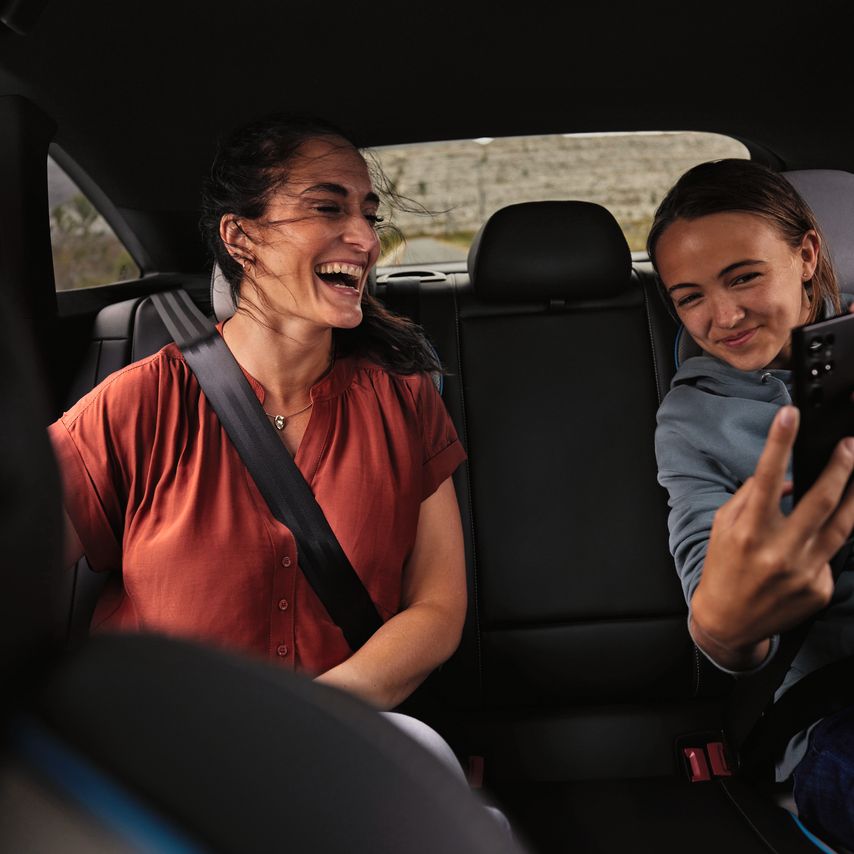 2 Peronen sitzen auf der Rückbank eines Volkswagen und schauen lächelnd auf ein Mobiltelefon