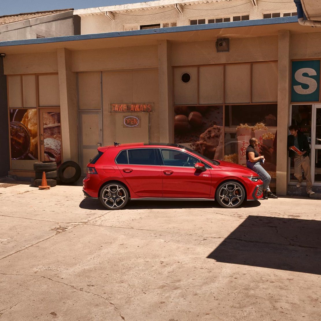 Seitenansicht eines roten VW Golf GTI, Frau lehnt an Motorhaube