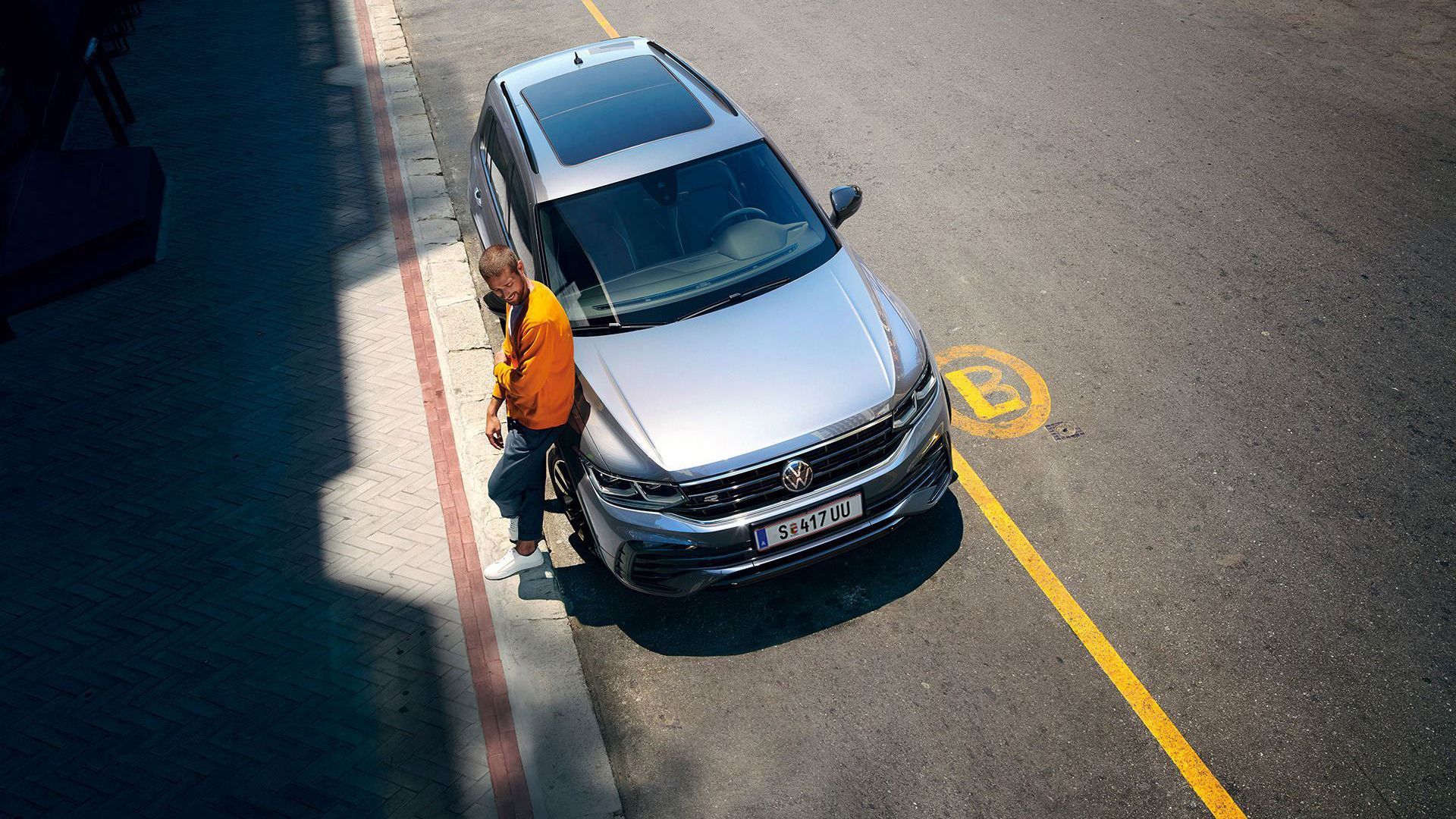 Ein Mann steht angelehnt am VW Tiguan, der geparkt am Straßenrand steht. 