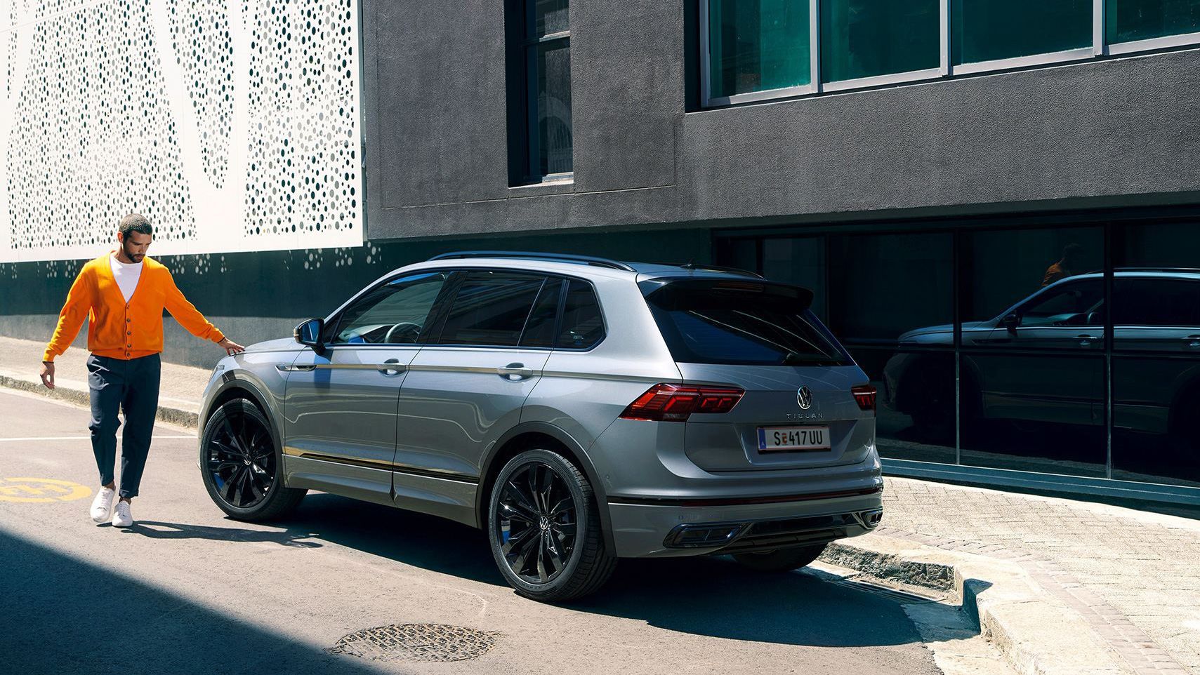 VW Tiguan R-Line in Grau Black Style von hinten. Mann steht daneben