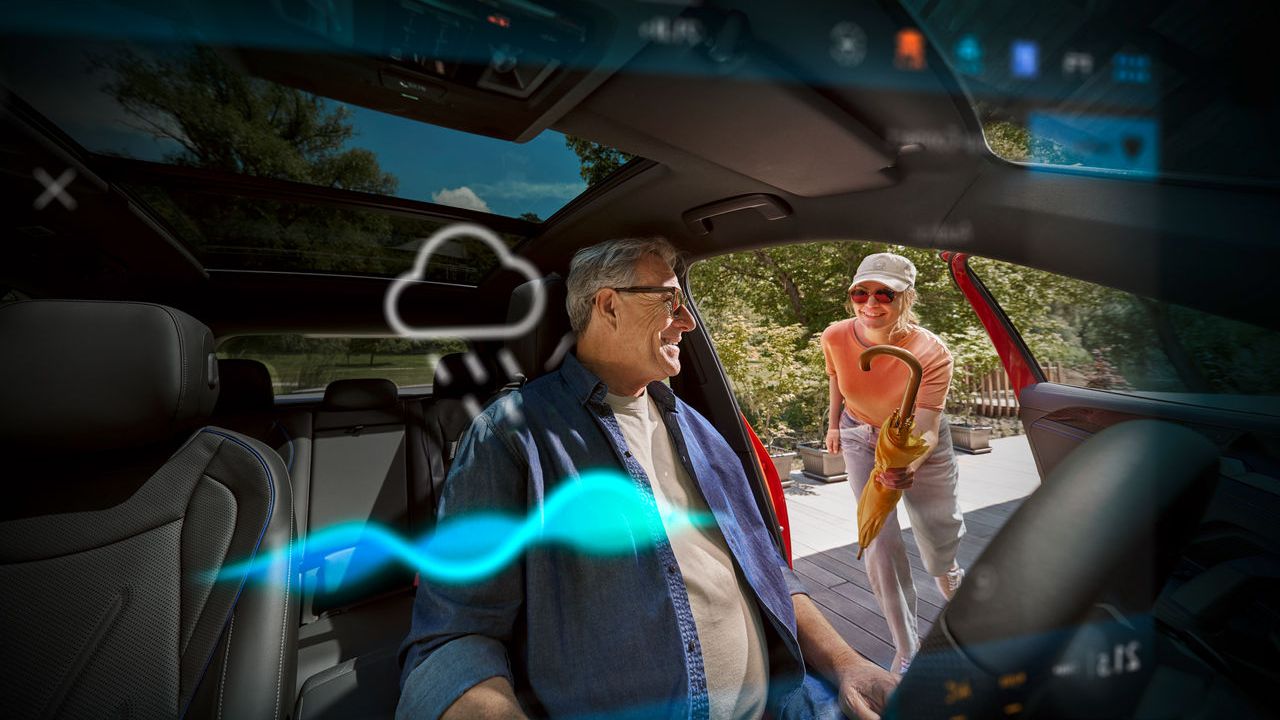 Älterer Mann sitz in seinem Volkswagen, eine Frau reicht ihm einen Regenschirm herein.