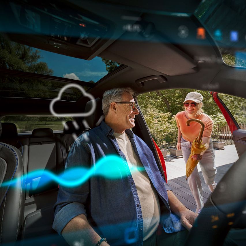 Älterer Mann sitz in seinem Volkswagen, eine Frau reicht ihm einen Regenschirm herein.