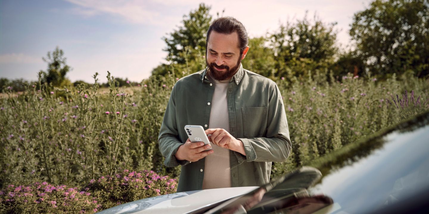  Ein Mann mit einem Smartphone in der Hand steht neben seinem ID.4