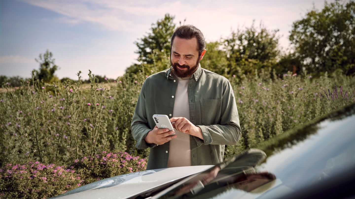  Ein Mann mit einem Smartphone in der Hand steht neben seinem ID.4