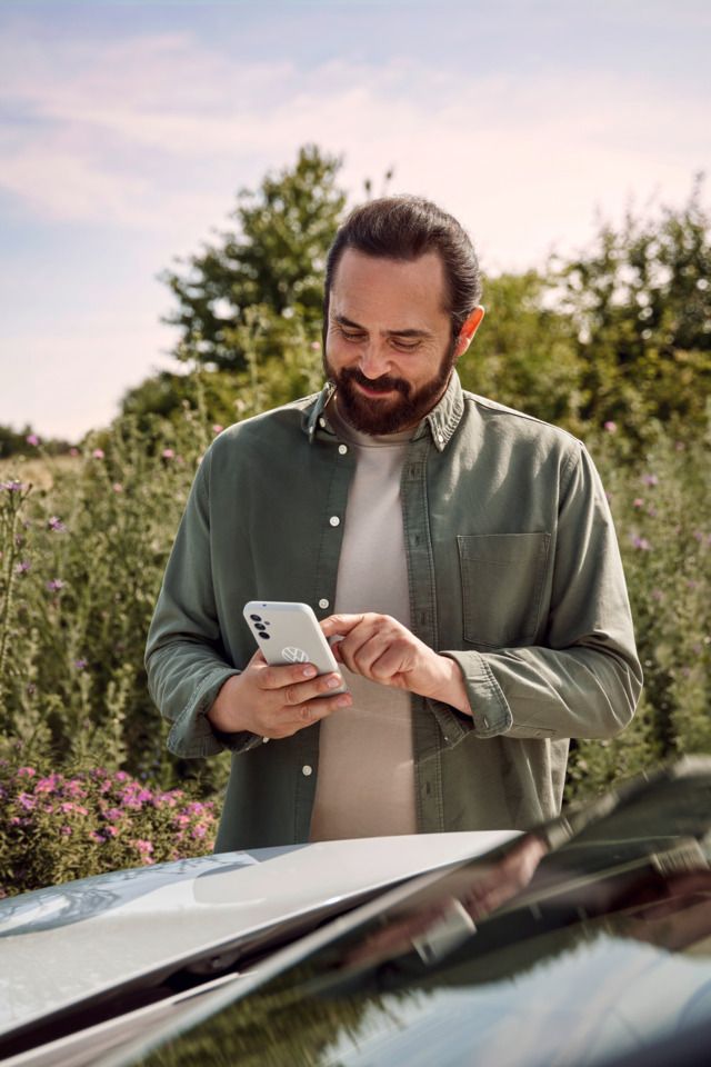  Ein Mann mit einem Smartphone in der Hand steht neben seinem ID.4