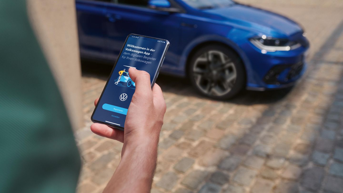  Eine Person hält ein Smartphone in der Hand mit der Volkswagen App, im Hintergrund steht ein blauer VW Polo R-Line.