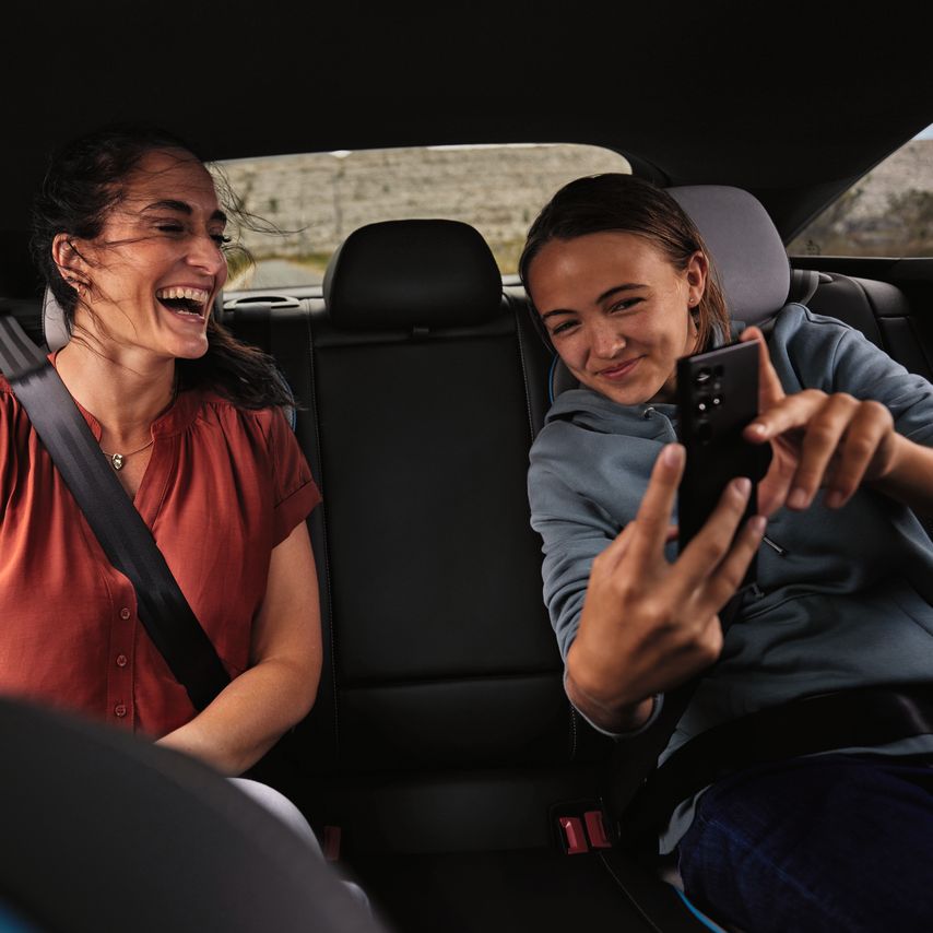 2 Peronen sitzen auf der Rückbank eines Volkswagen und schauen lächelnd auf ein Mobiltelefon