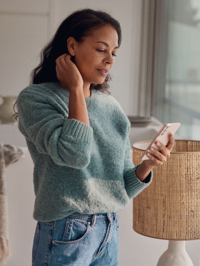 Eine Frau steht am Fenster und blickt auf ihr Smartphone