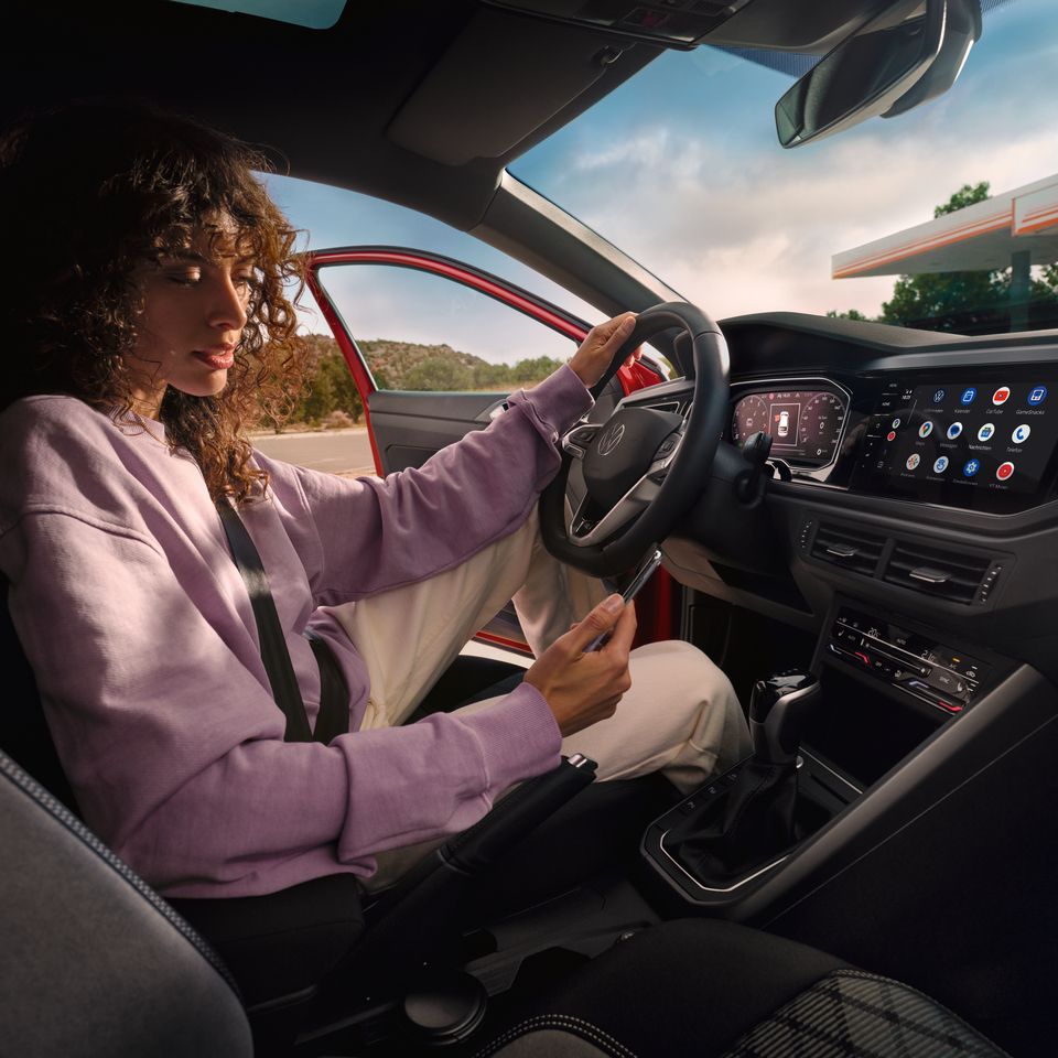 Eine Frau sitzt in ihrem geparkten VW Taigo und schaut auf ihr Handy