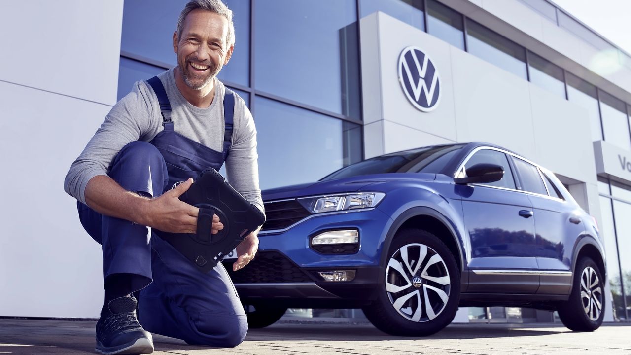 Ein Volkswagen Service Techniker mit Tablet, kniet vor einem blauen Volkswagen T-Roc