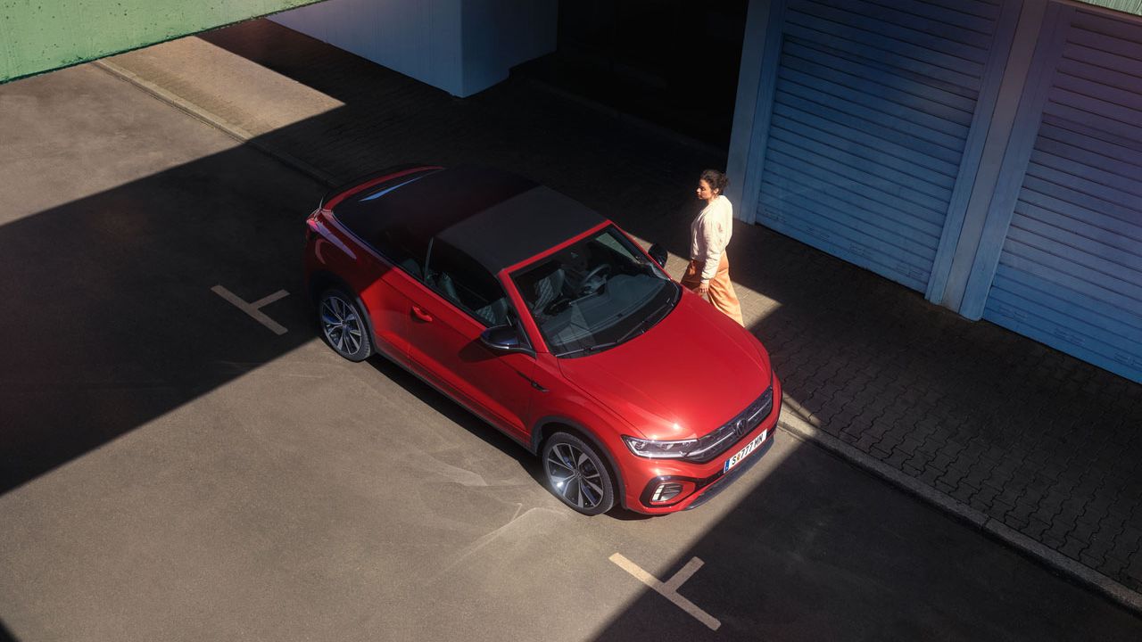 Eine Frau läuft zu einem geparkten VW T-Roc Cabriolet, Ansicht von schräg/oben