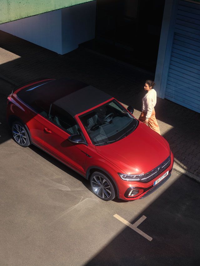 Eine Frau läuft zu einem geparkten VW T-Roc Cabriolet, Ansicht von schräg/oben