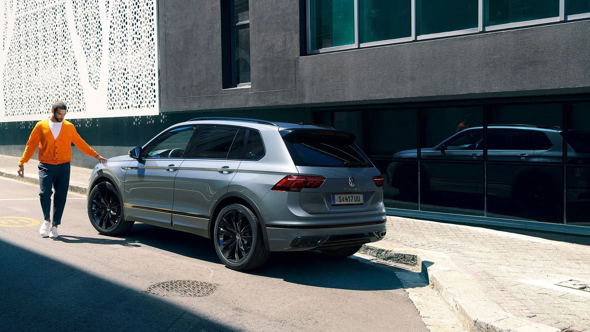 VW Tiguan R-Line in Grau Black Style von hinten. Mann steht daneben