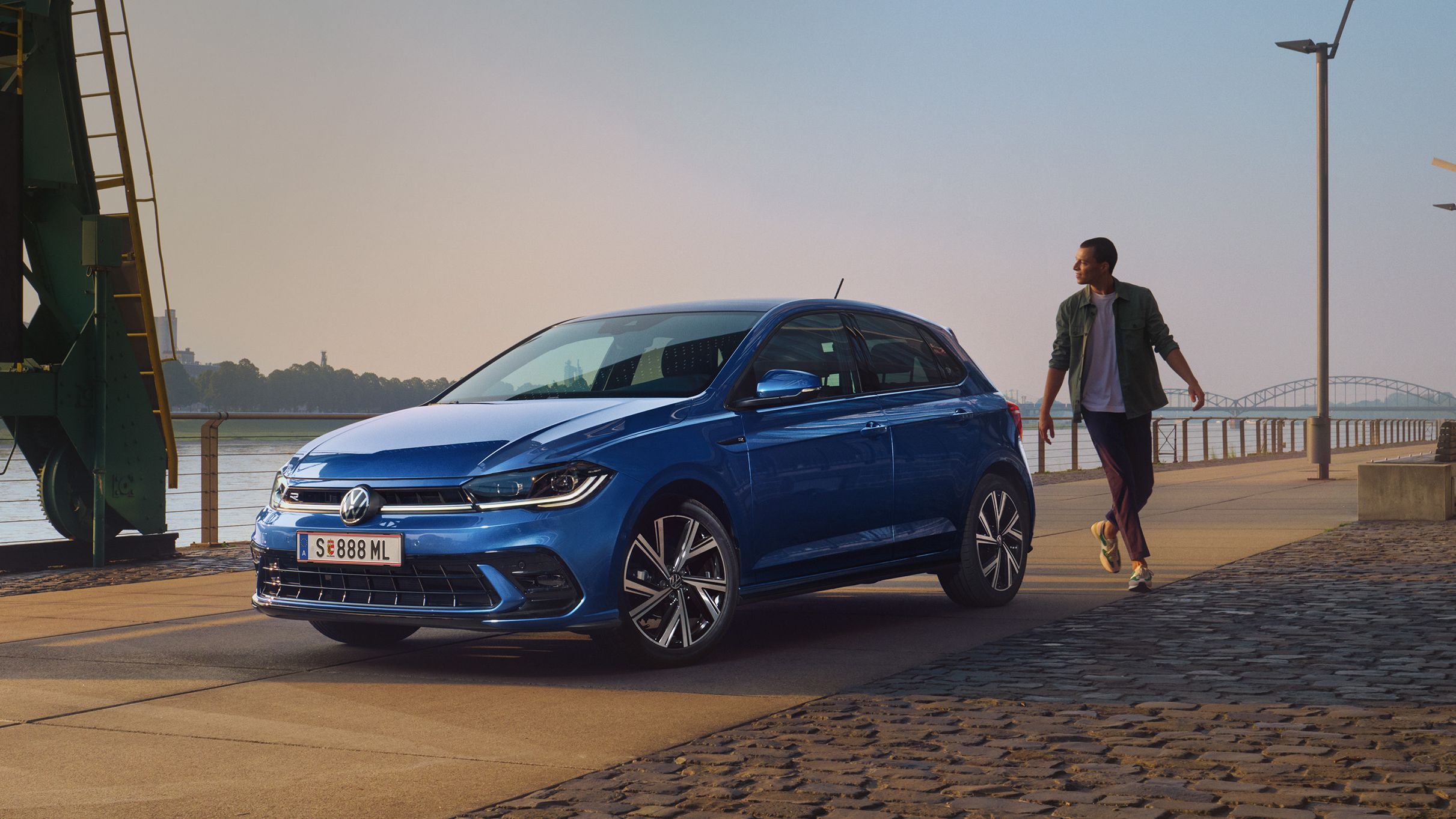 Mann geht an blauen VW Polo R-Line vorbei, der an Promenade geparkt ist