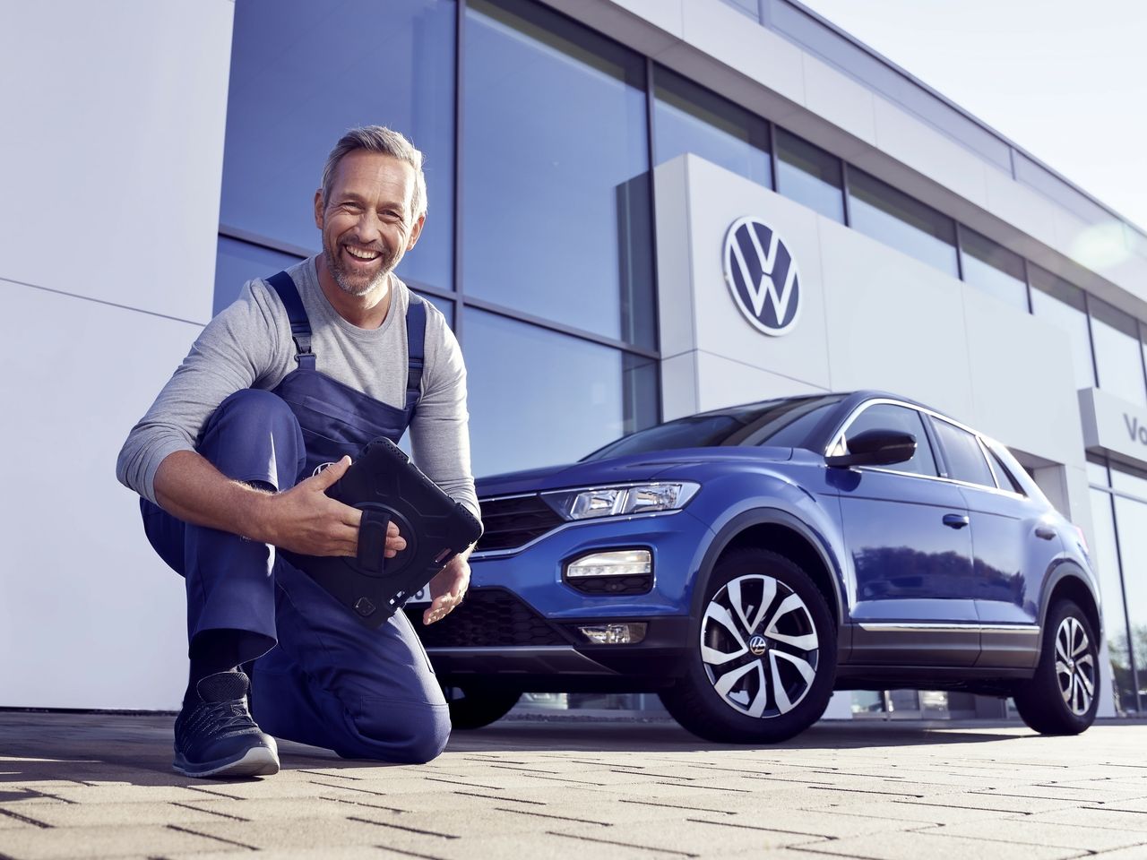 Ein Volkswagen Service Techniker mit Tablet, kniet vor einem blauen Volkswagen T-Roc