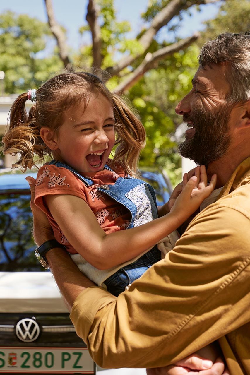 Ein Vater hält Kind im Arm, beide lachen, man sieht das Heck des VW ID.7