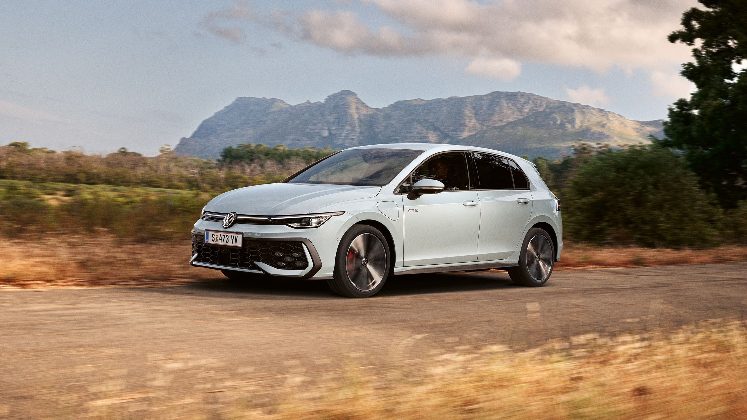 Der VW Golf GTE fährt auf einer Landstraße, im Hintergrund sieht man Berge