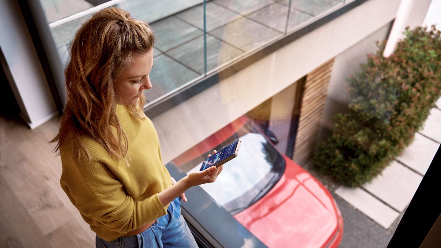 Frau schaut zu Hause auf ihr Smartphone, während ihr Tiguan in der Einfahrt geparkt ist