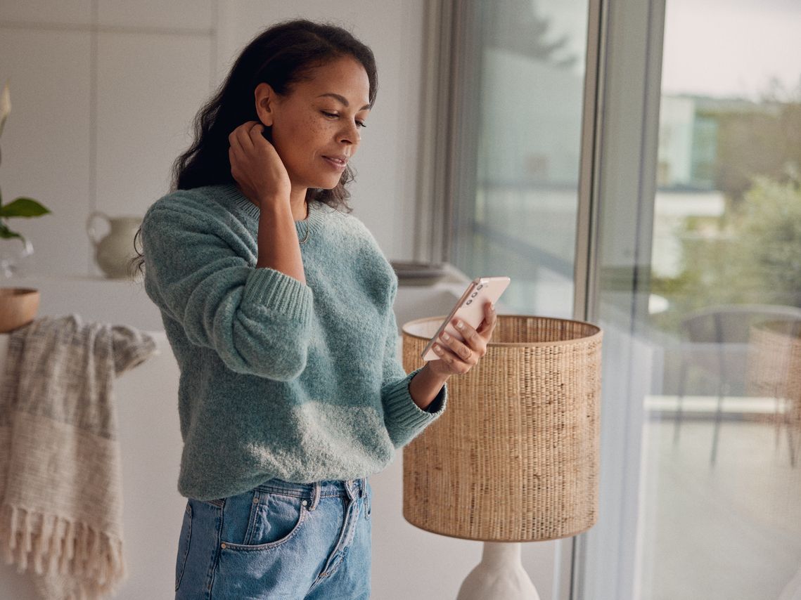 Eine Frau steht am Fenster und blickt auf ihr Smartphone