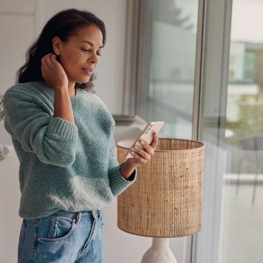 Eine Frau steht am Fenster und blickt auf ihr Smartphone