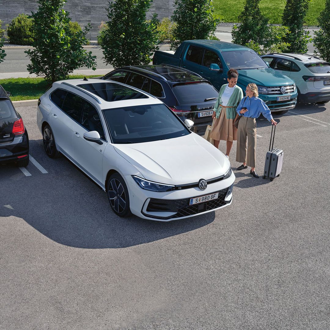 Zwei Frauen stehen auf einem Parkplatz neben einem weißen VW Passat B9