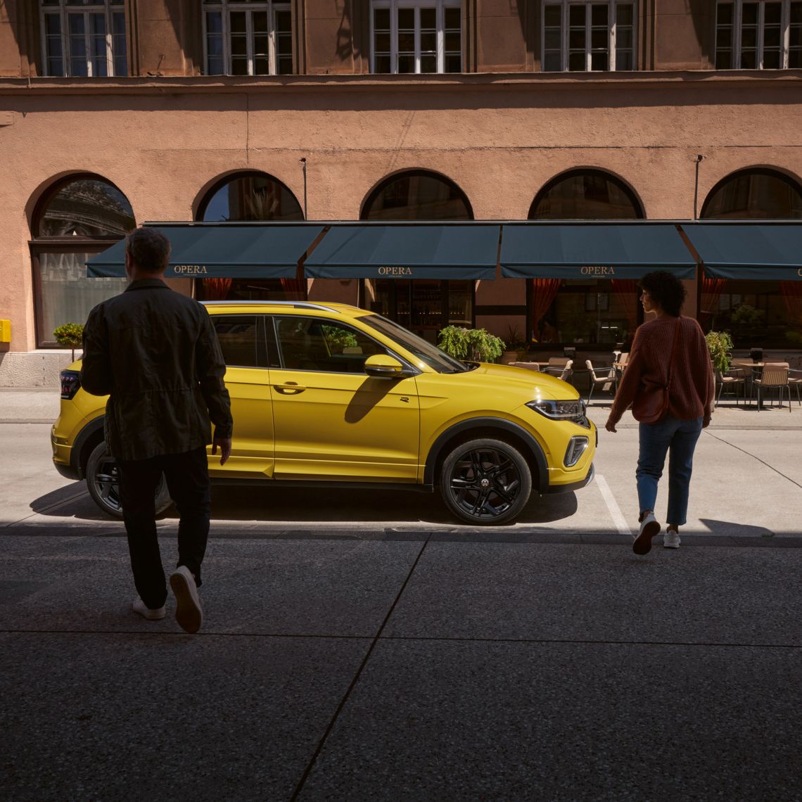 Mann und Frau nähern sich einem gelben VW T-Cross am Straßenrand.