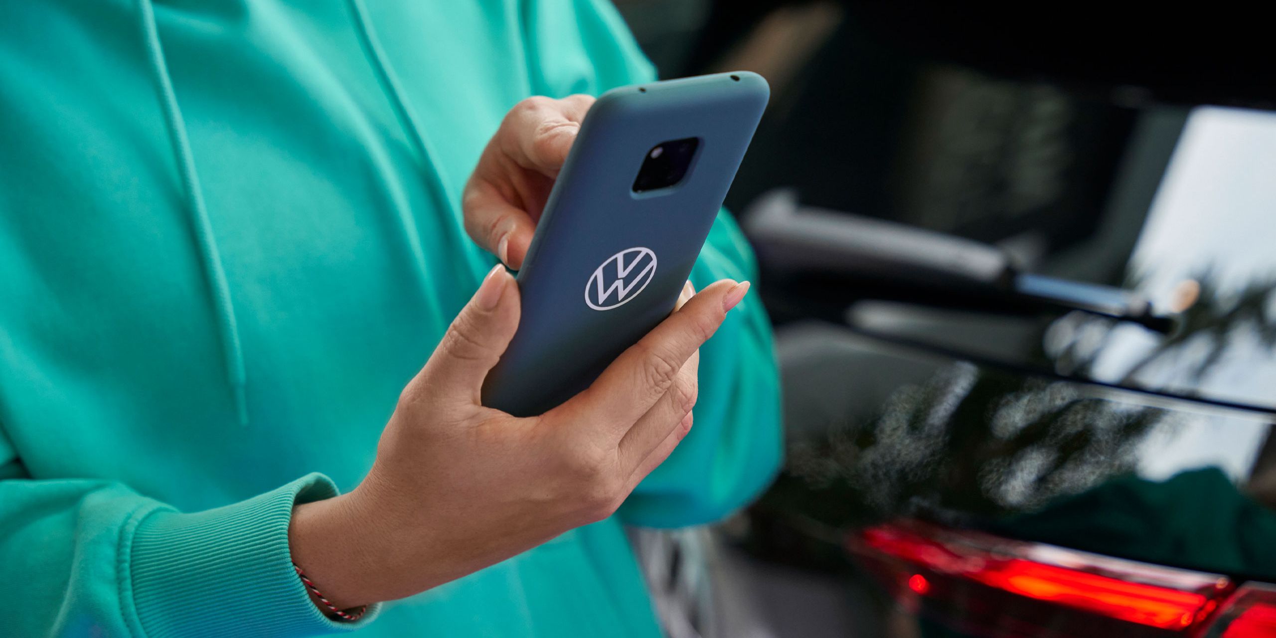 Eine Frau tippt in ihr Smartphone. Auf der blauen Schutzhülle ist das Volkswagen Logo abgebildet.