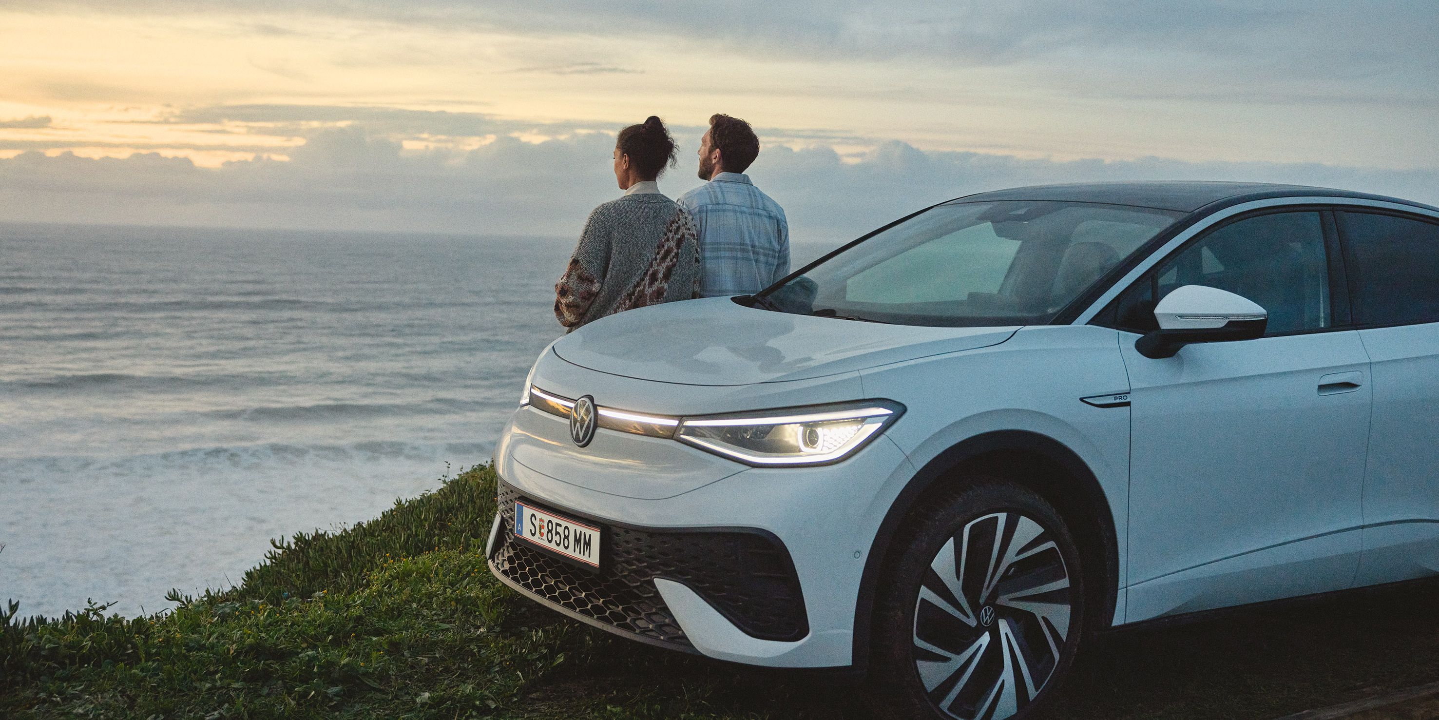 Ein ID.5 steht auf einer Wiese, der Blick geht aufs Meer. Ein Paar steht am Auto und blickt auf das Meer.