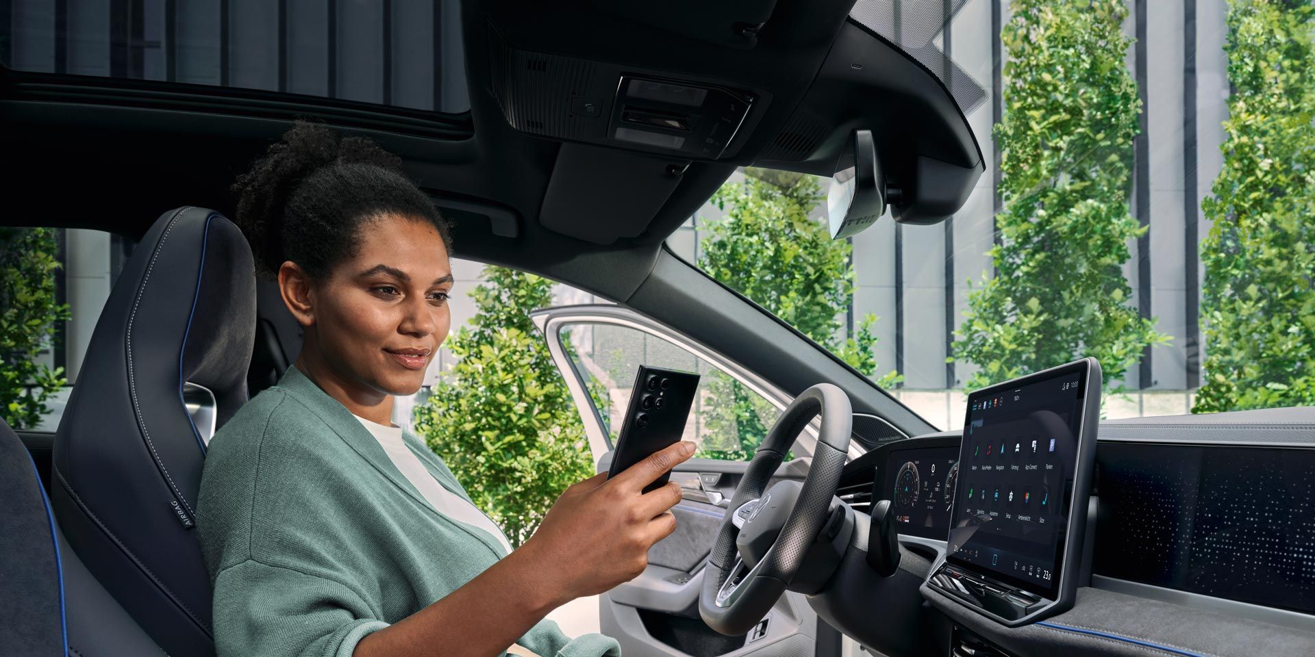 Eine Frau sitzt bei geöffneter Tür auf dem Fahrersitz des geparkten VW Passat und blickt auf ihr Smartphone.