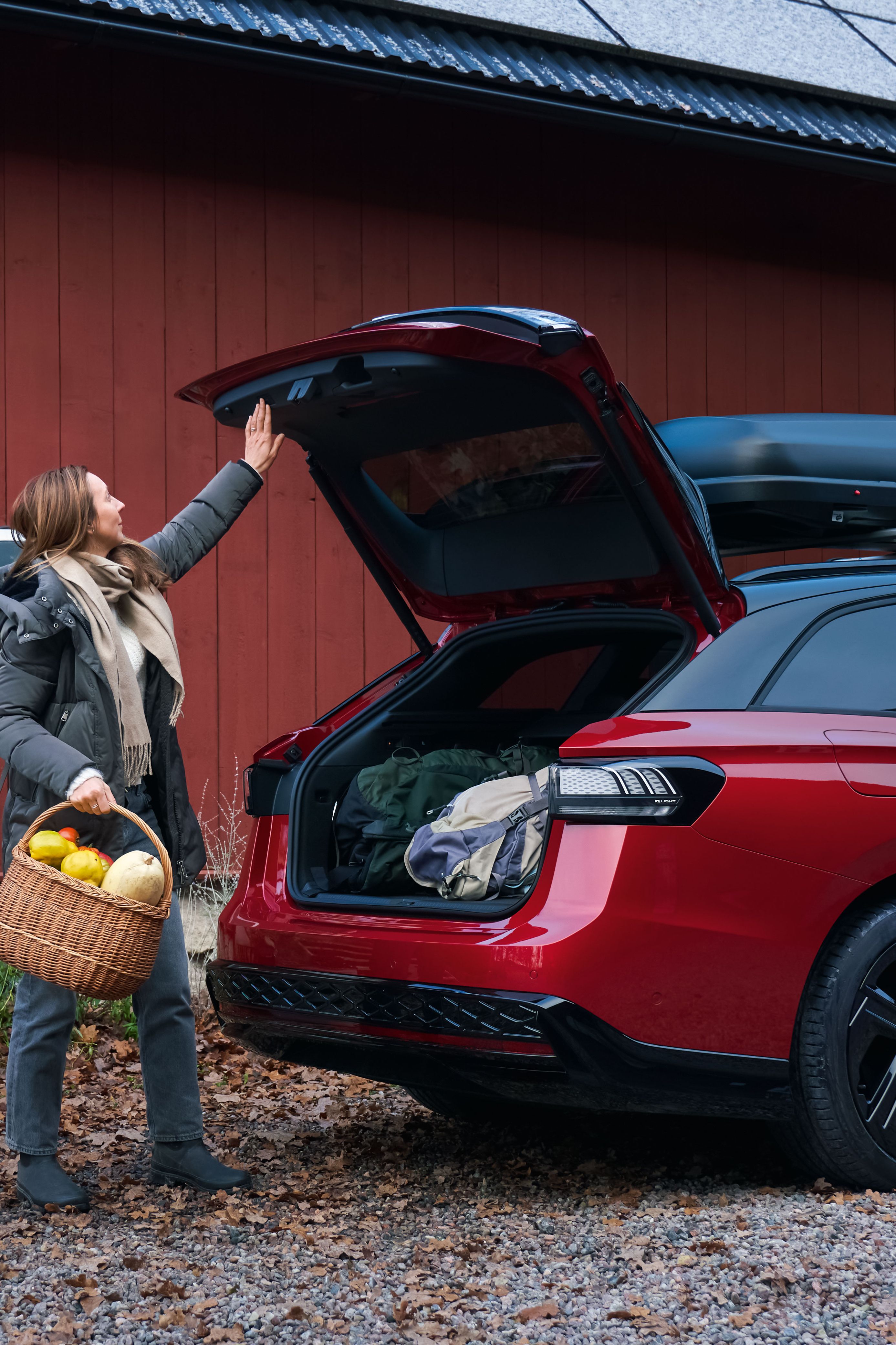 Ein roter Volkswagen Passat mit Dachbox, eine Frau mit Obstkorb in der Hand schließt den Kofferraum